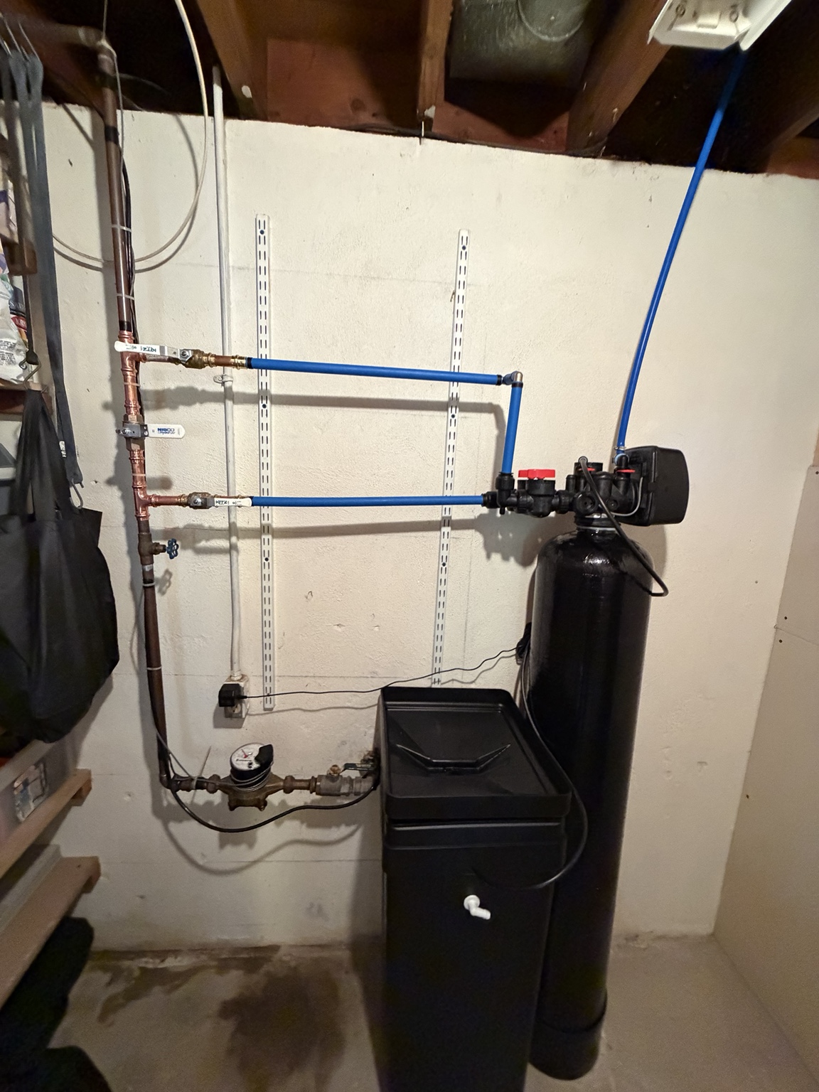 Black water softener with a digital control head and brine tank connected to copper and blue piping.